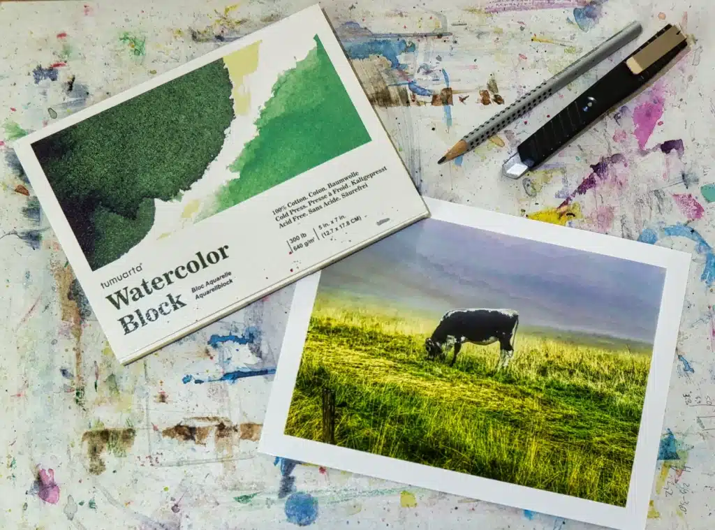 Foto einer Kuh und Aquarellblock auf gesprenkelter Malunterlage.